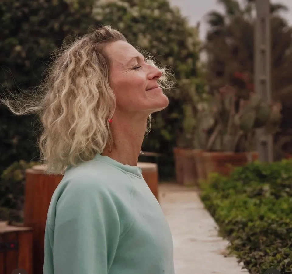 Side profile of a smiling woman with curly blonde hair practising mindful breathing outdoors