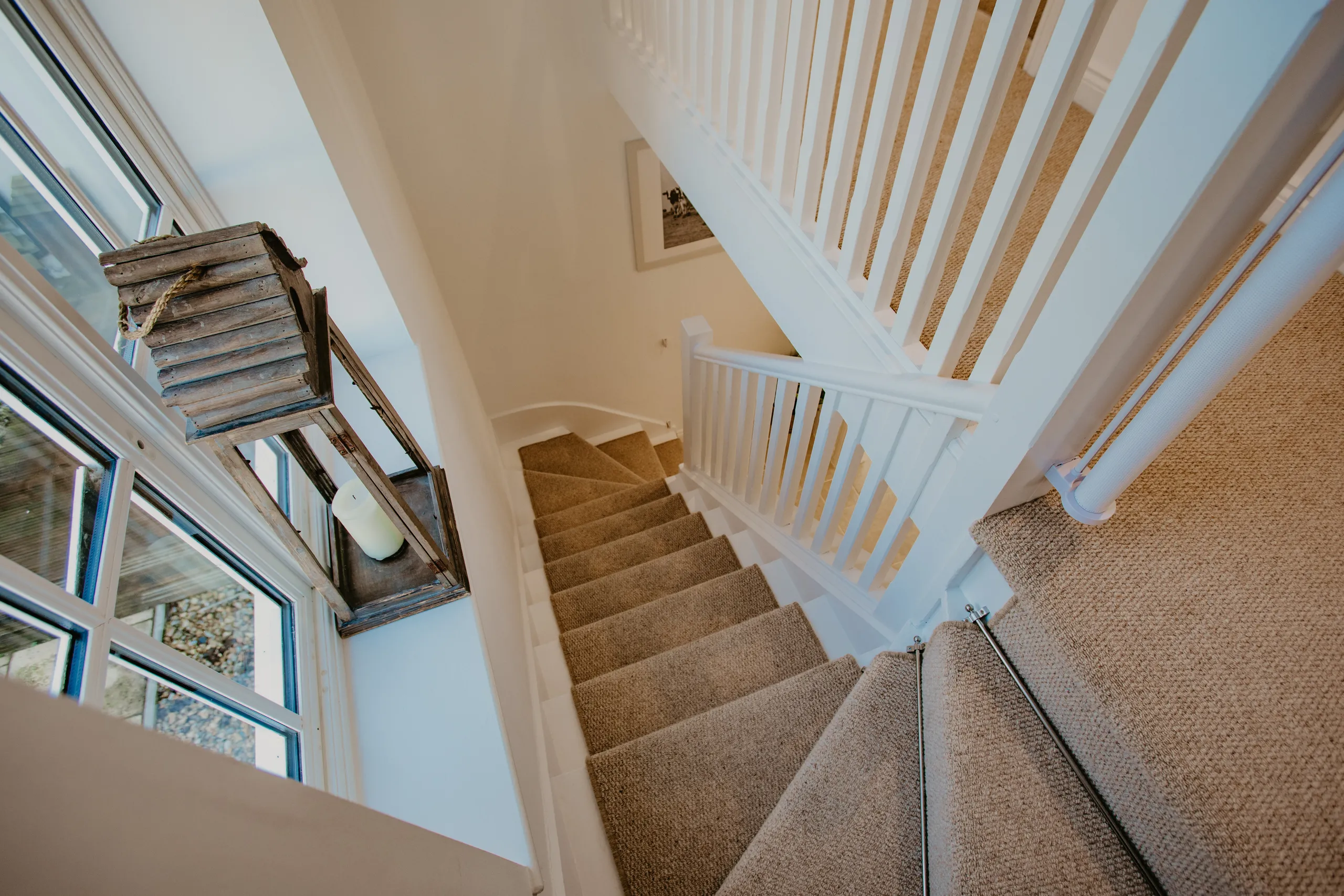 Carpeted staircase with white banister and large window, viewed from above