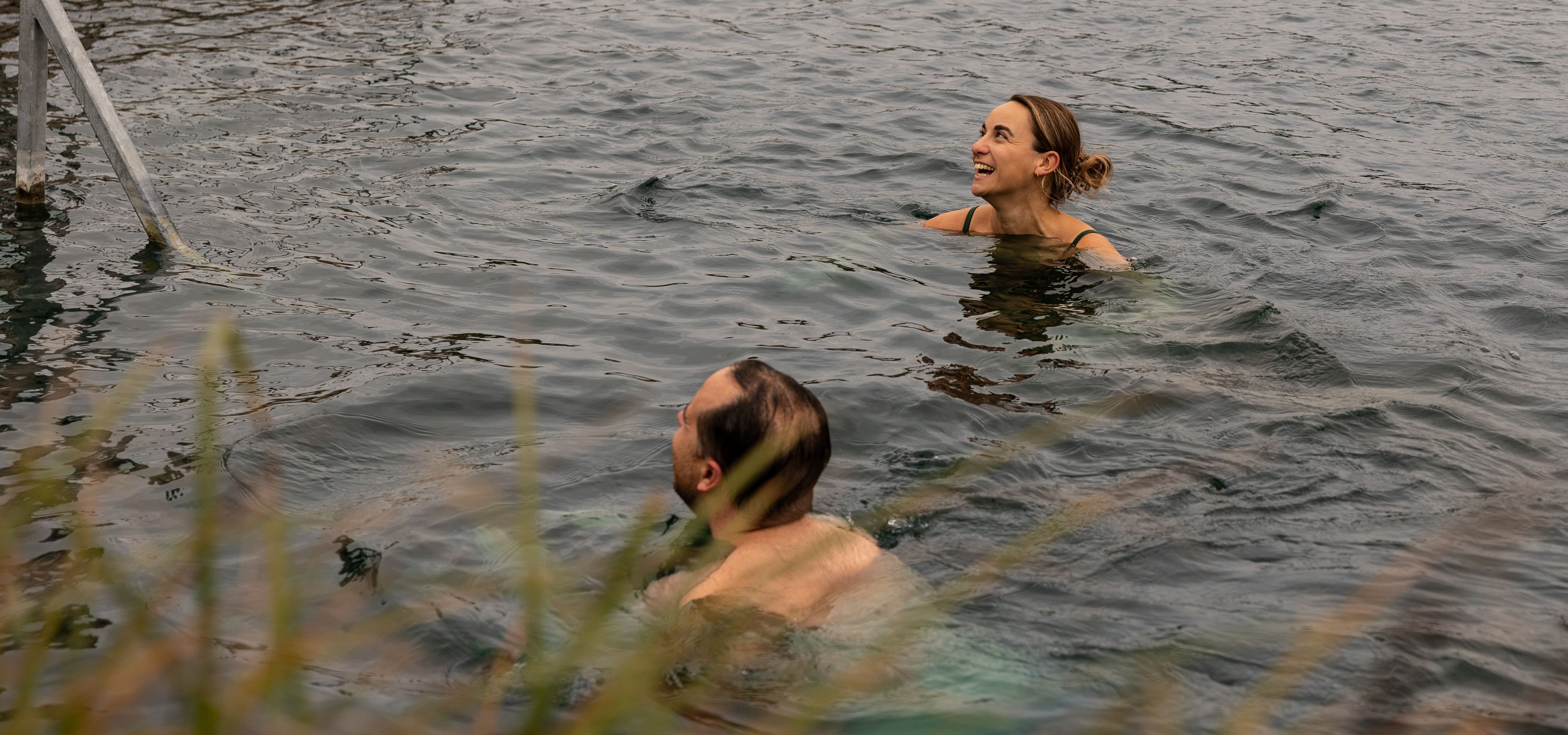 Two people swimming in open water near a metal ladder