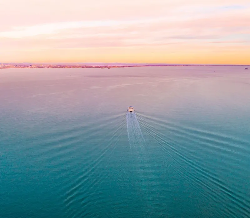 Aerial view of a small boat leaving a wake across calm blue sea at sunset