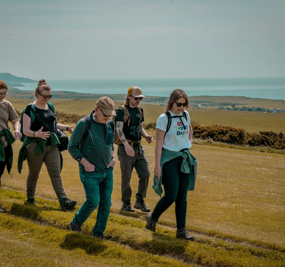 Group of walkers on a grassy coastal trail with sea views in the distance