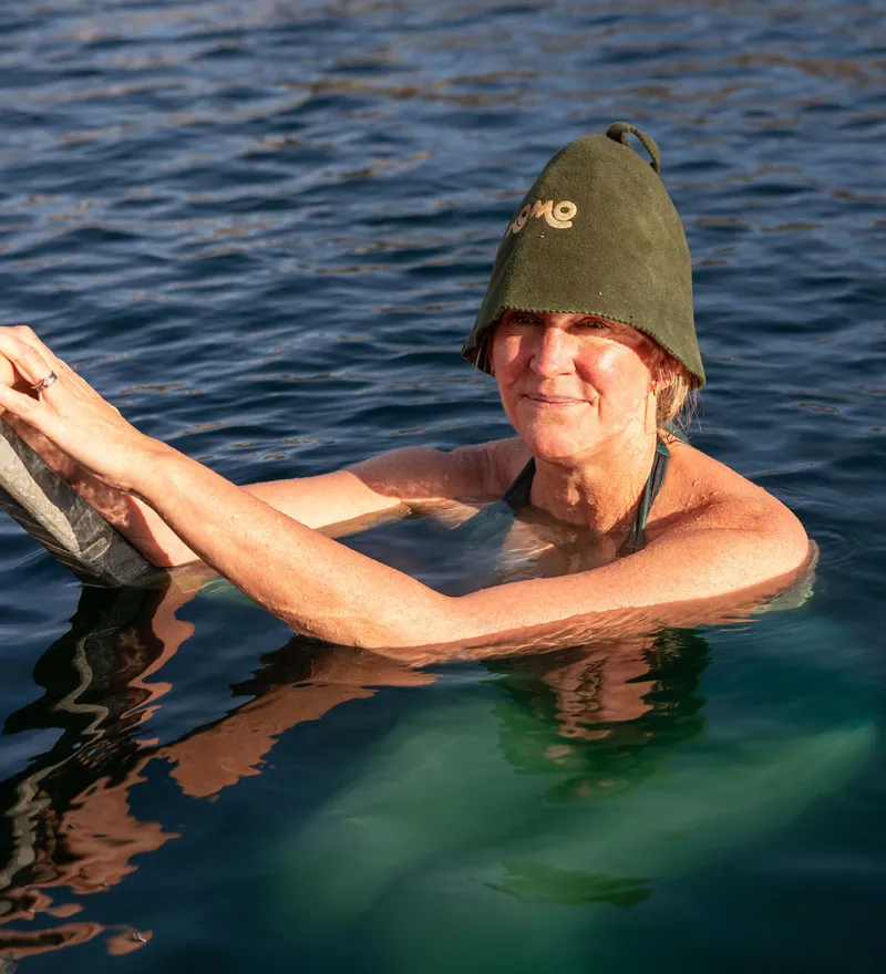 Woman in a green swim hat holding a metal ladder in open water