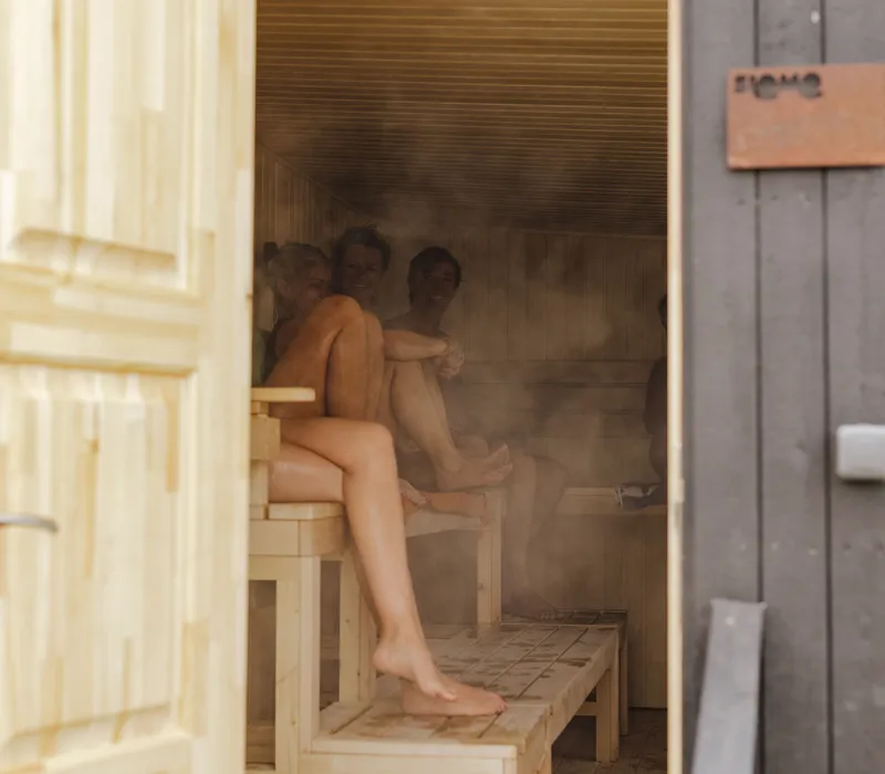 People relaxing in a steaming outdoor sauna, viewed through an open wooden door