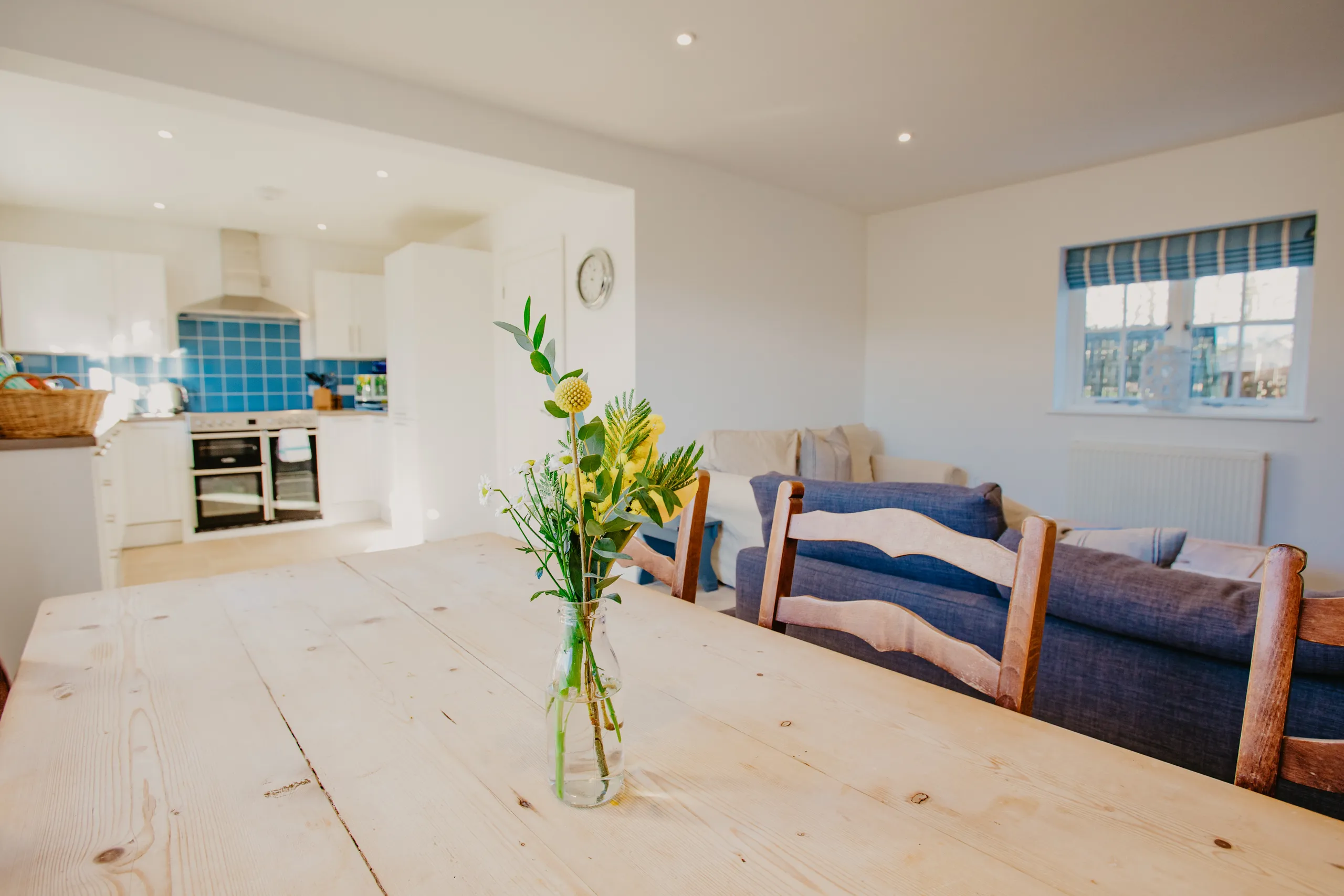 Bright open-plan kitchen and living area with wooden dining table and vase of flowers