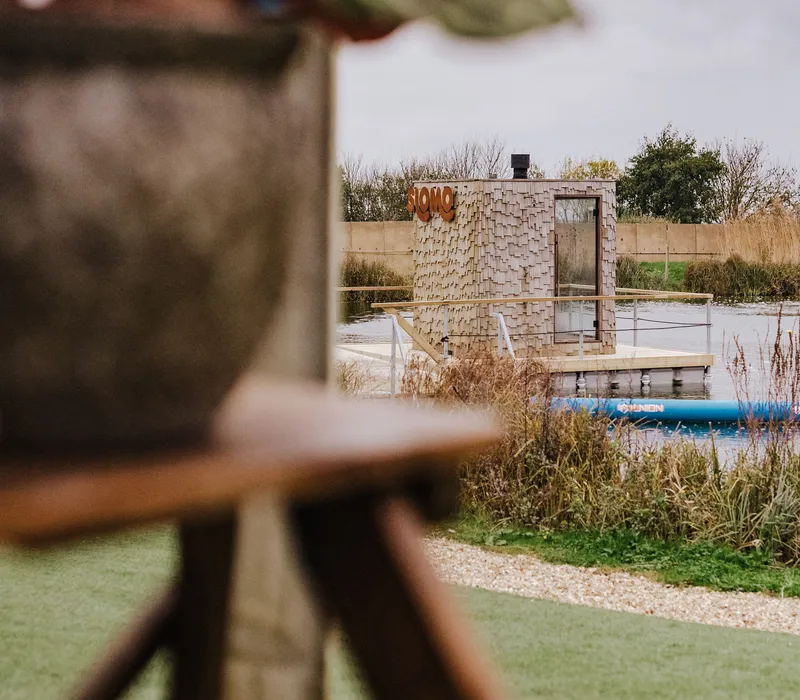 Wood-clad Slomo sauna hut on a floating pontoon beside a lake at Tapnell Farm