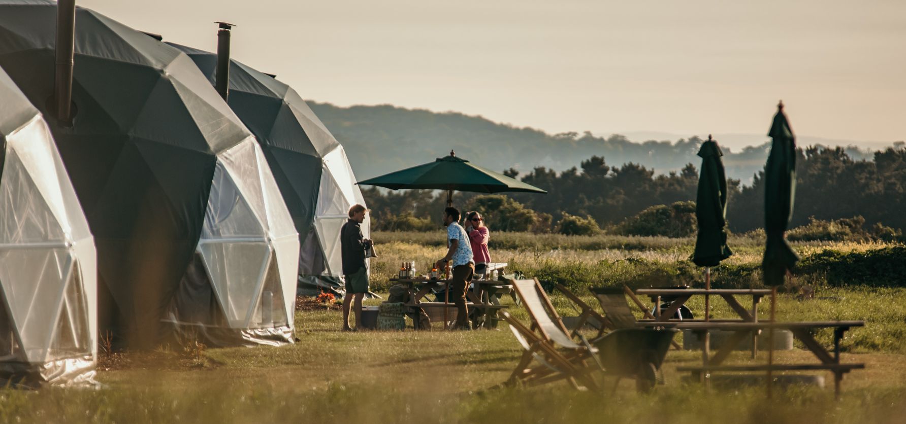 Geodesic dome eco lodges with outdoor picnic table and parasols in a sunny field at Tapnell Farm