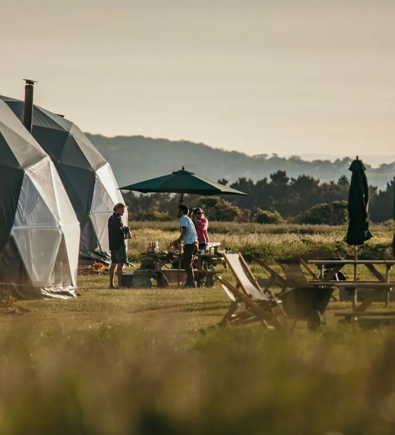 Geodesic dome eco lodges with outdoor picnic table and parasols in a sunny field at Tapnell Farm