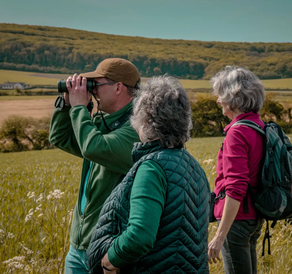Group of walkers on a countryside hillside, one using binoculars to look across fields