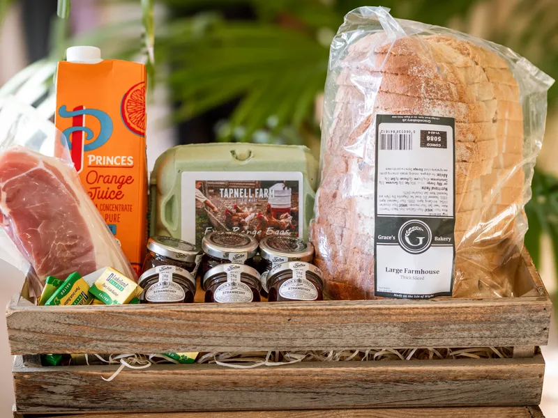 Wooden breakfast hamper with sliced bread, orange juice, eggs, jam, butter and bacon