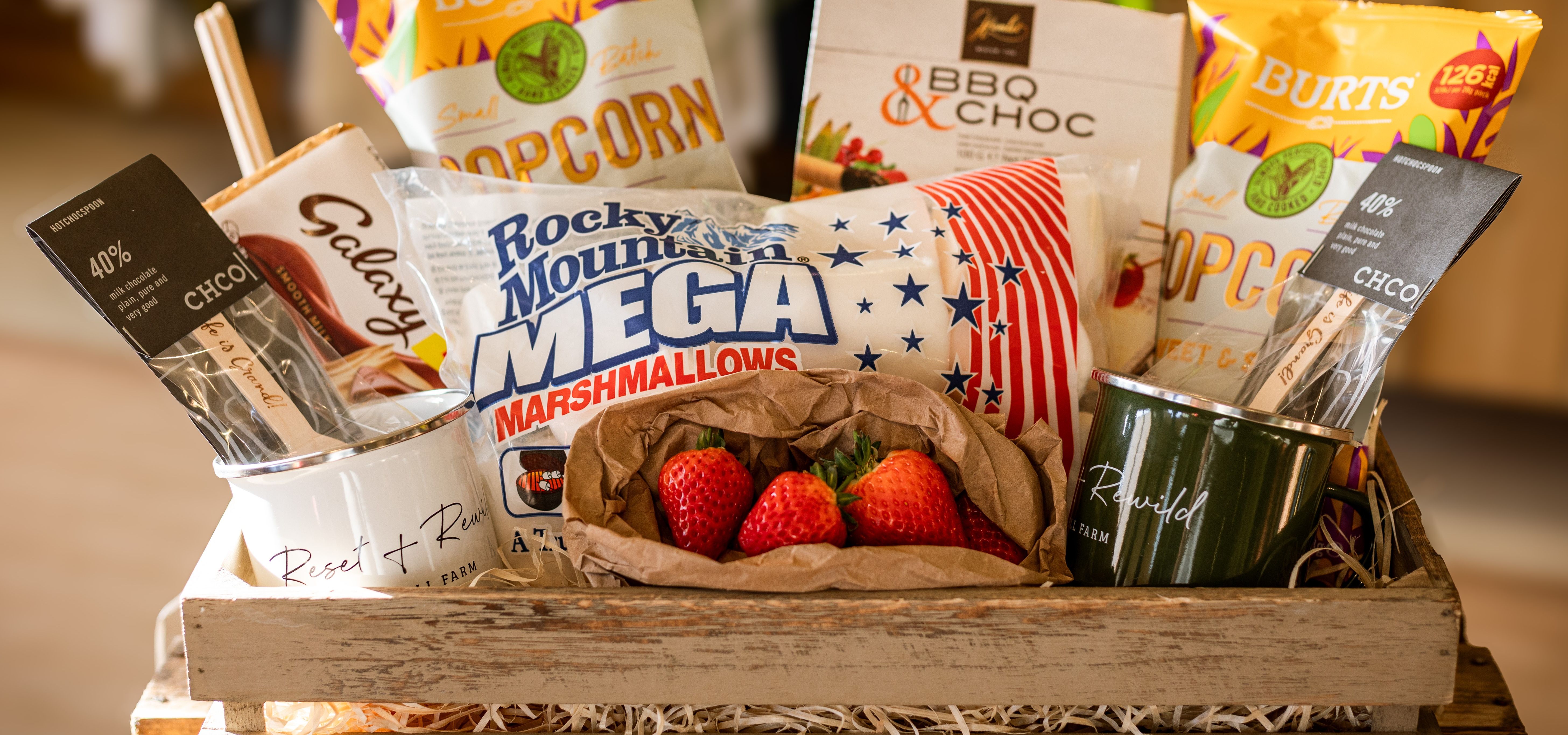 Gift hamper with popcorn, marshmallows, chocolate and fresh strawberries in a wooden crate