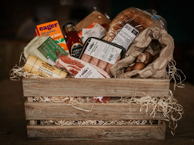 Wooden crate filled with groceries including eggs, butter, sausages, bacon, bread, ketchup, orange juice and mushrooms