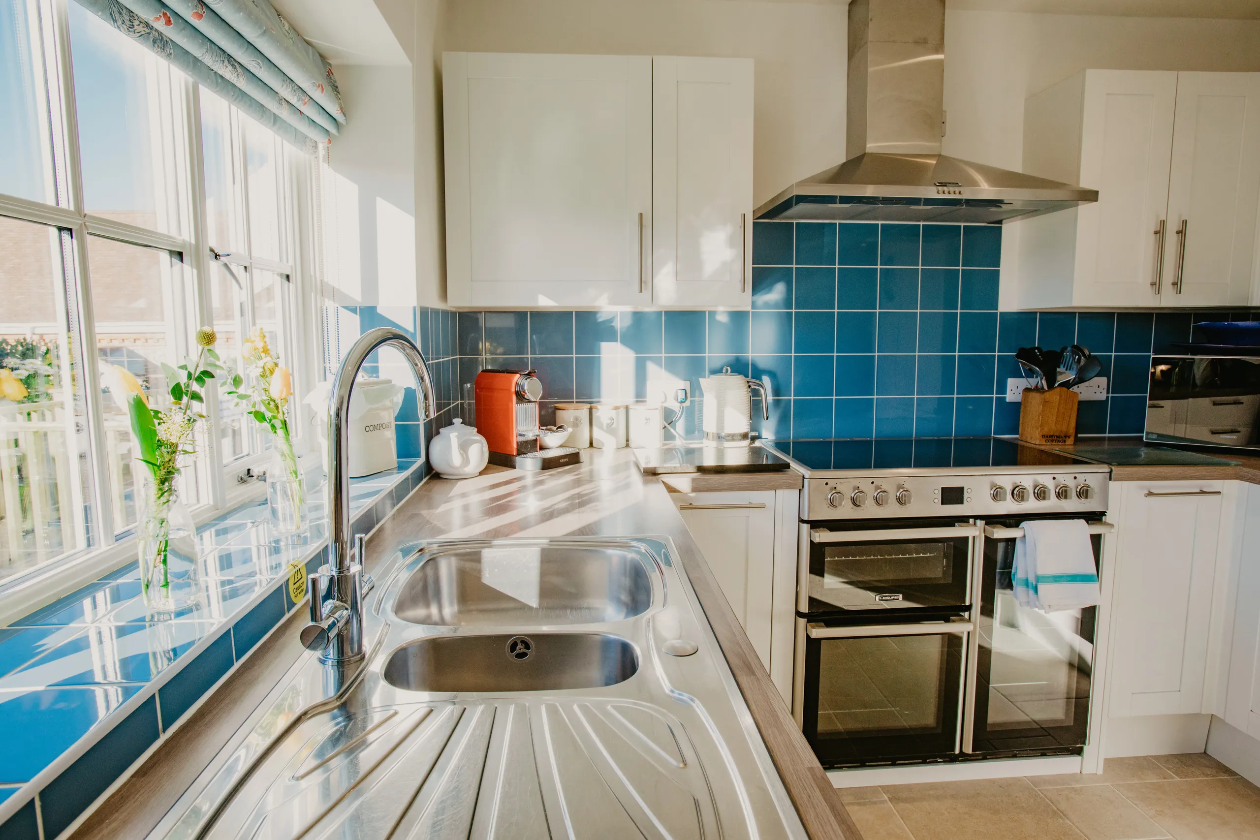 Sunlit modern kitchen with blue tiled splashback, double sink and range cooker