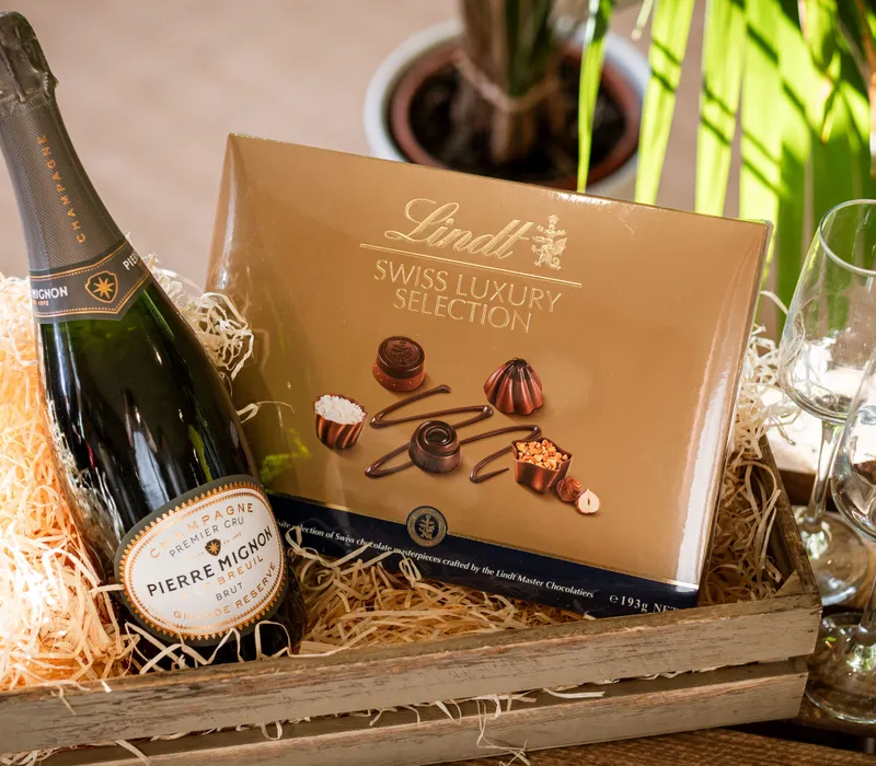 Champagne bottle and Lindt Swiss Luxury Selection chocolates in a wooden gift crate with two glasses