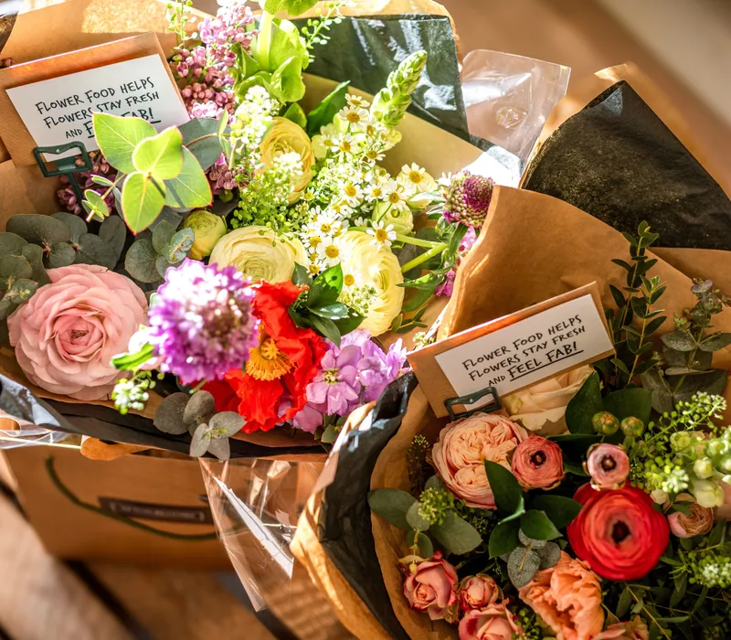 Two colourful bouquets of mixed flowers wrapped in brown paper with greenery and small gift cards