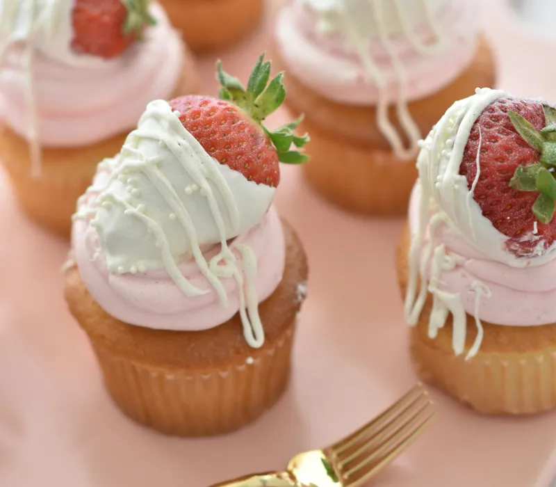 Strawberry cupcakes with pink frosting and white chocolate-dipped strawberries on a pink plate