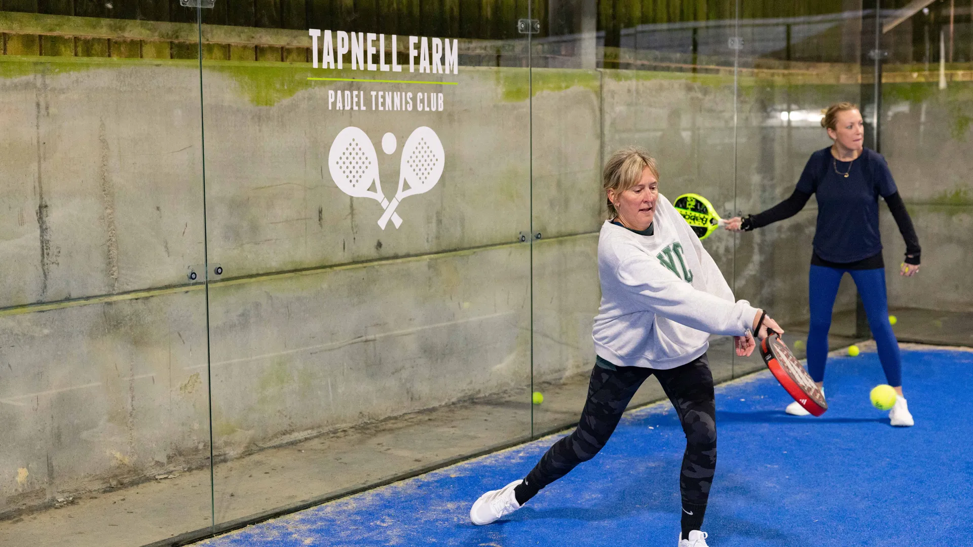 Two women playing padel on an indoor court at Tapnell Farm Padel Tennis Club