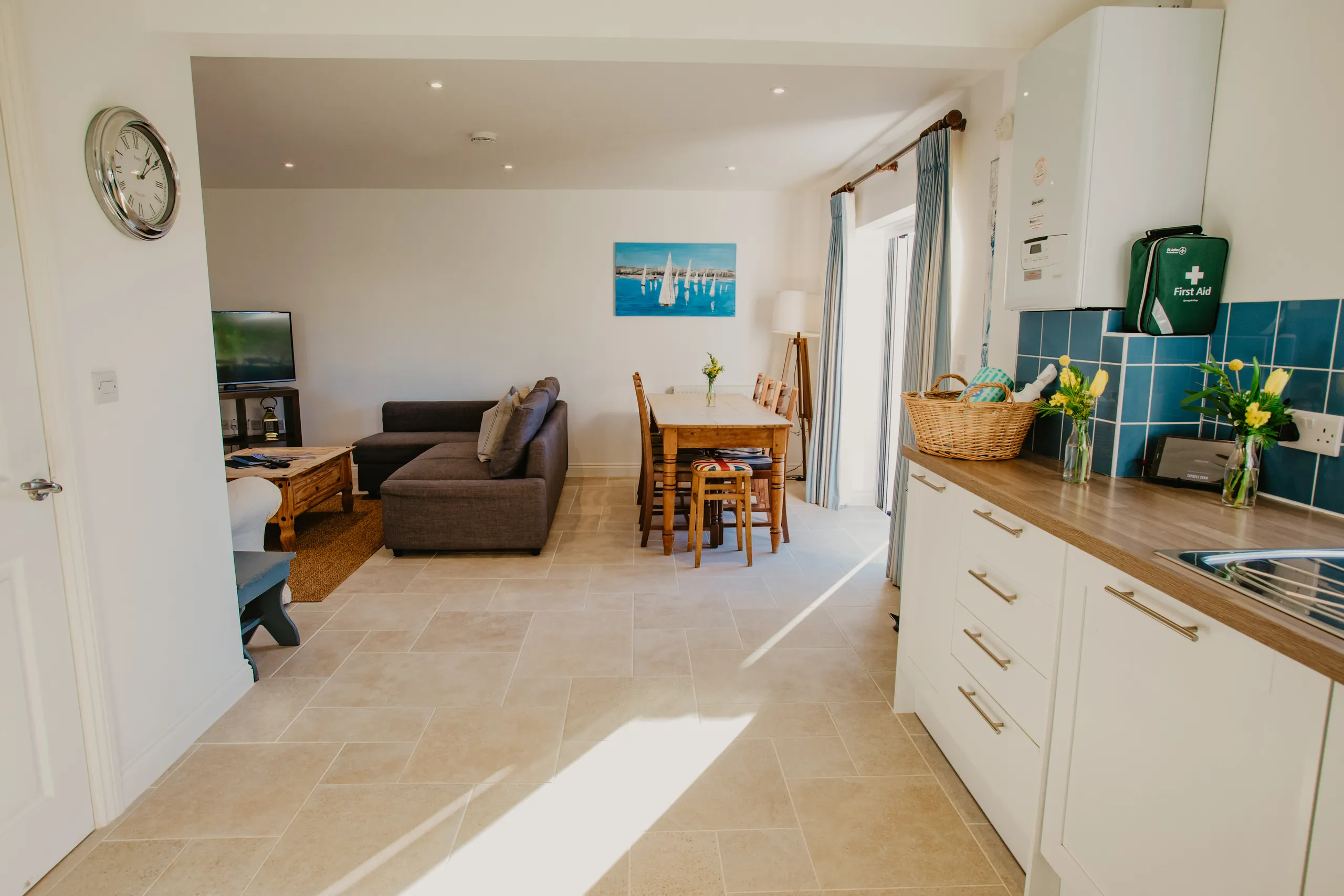 Open-plan kitchen, dining and lounge area with grey sofa, wooden dining table and blue tiled splashback