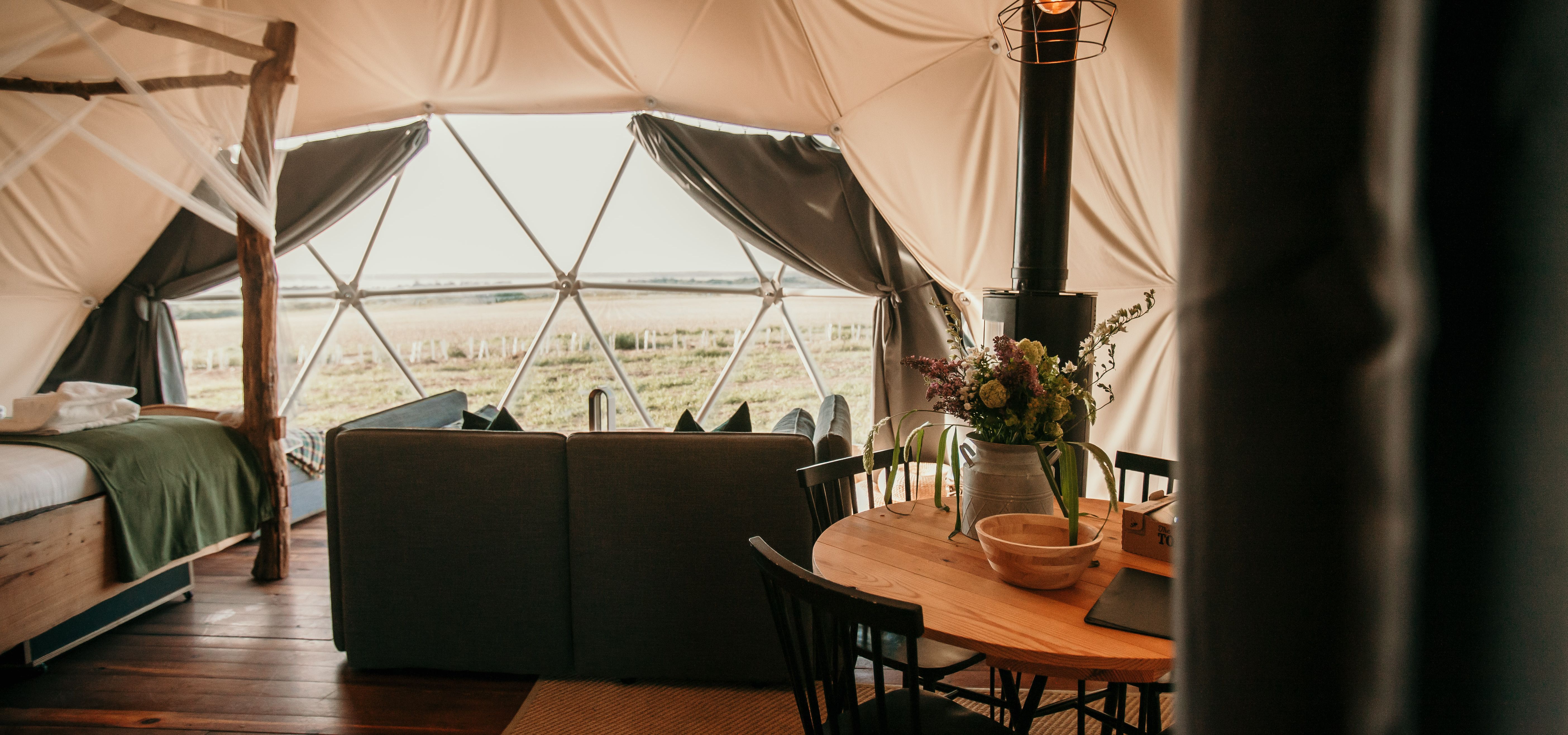 Cosy living area inside the Tapnell Farm Dome Meadow glamping dome with sofa, dining table, wood burner and countryside view