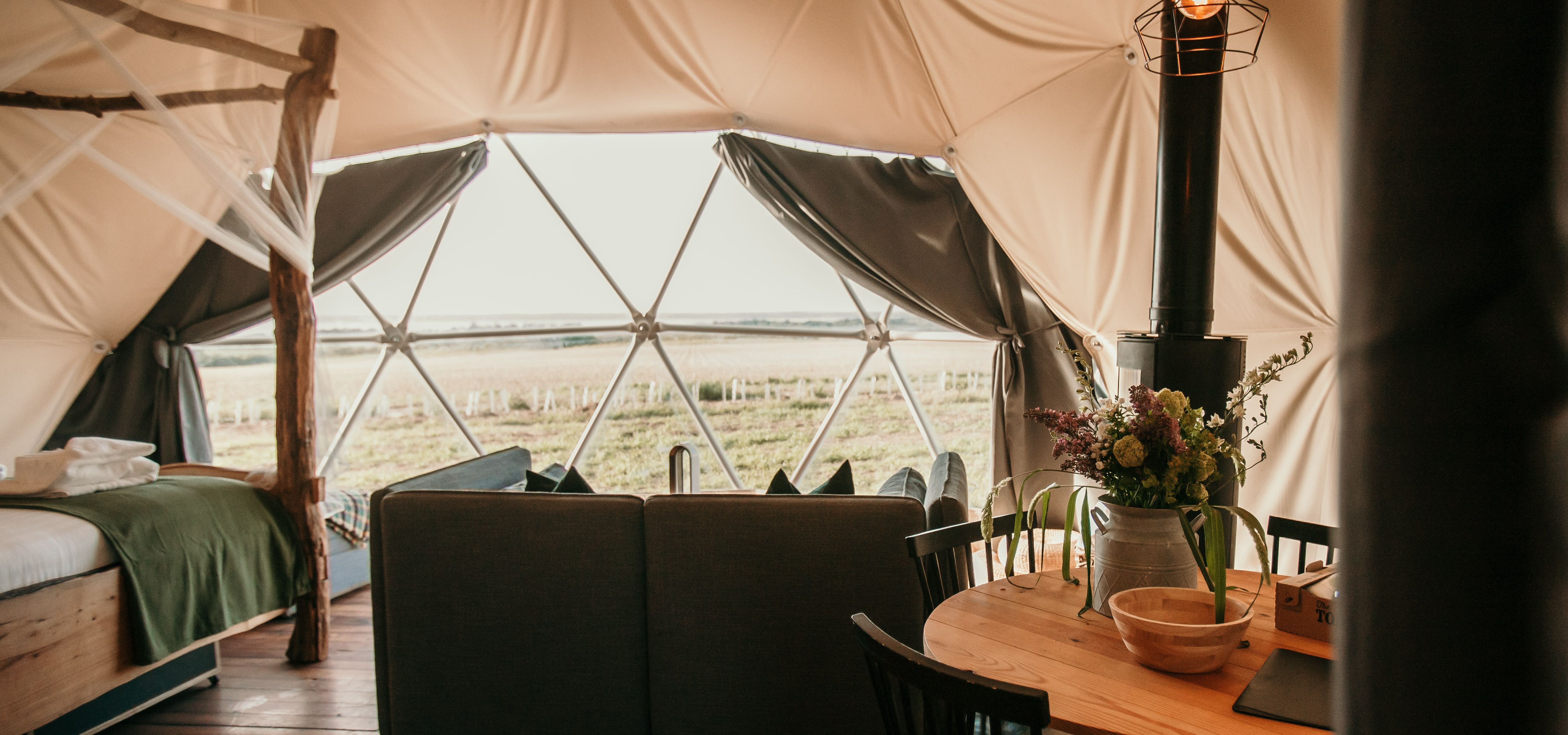 Cosy living area inside the Tapnell Farm Dome Meadow glamping dome with sofa, dining table, wood burner and countryside view
