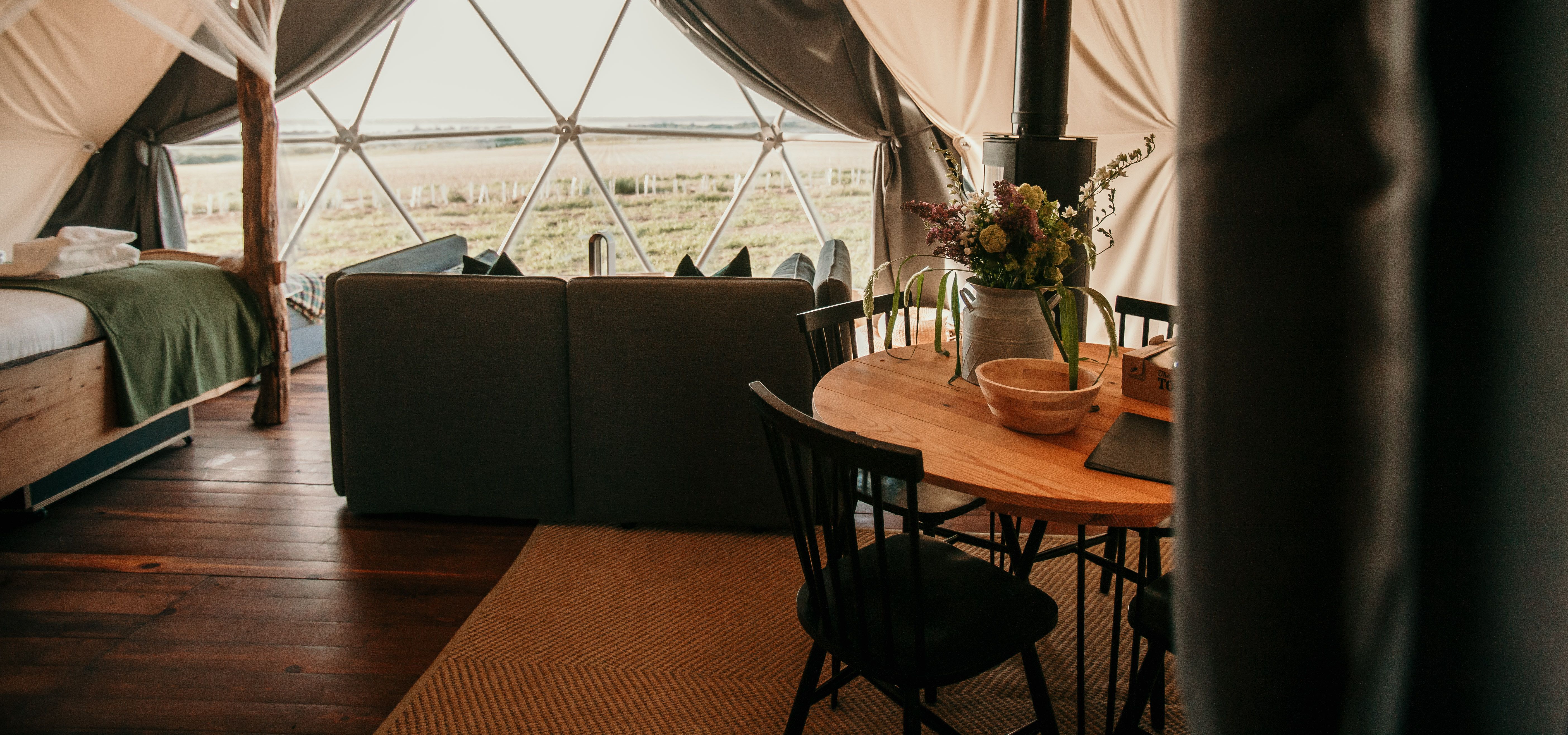Cosy living area inside the Tapnell Farm Dome Meadow glamping dome with sofa, dining table, wood burner and countryside view