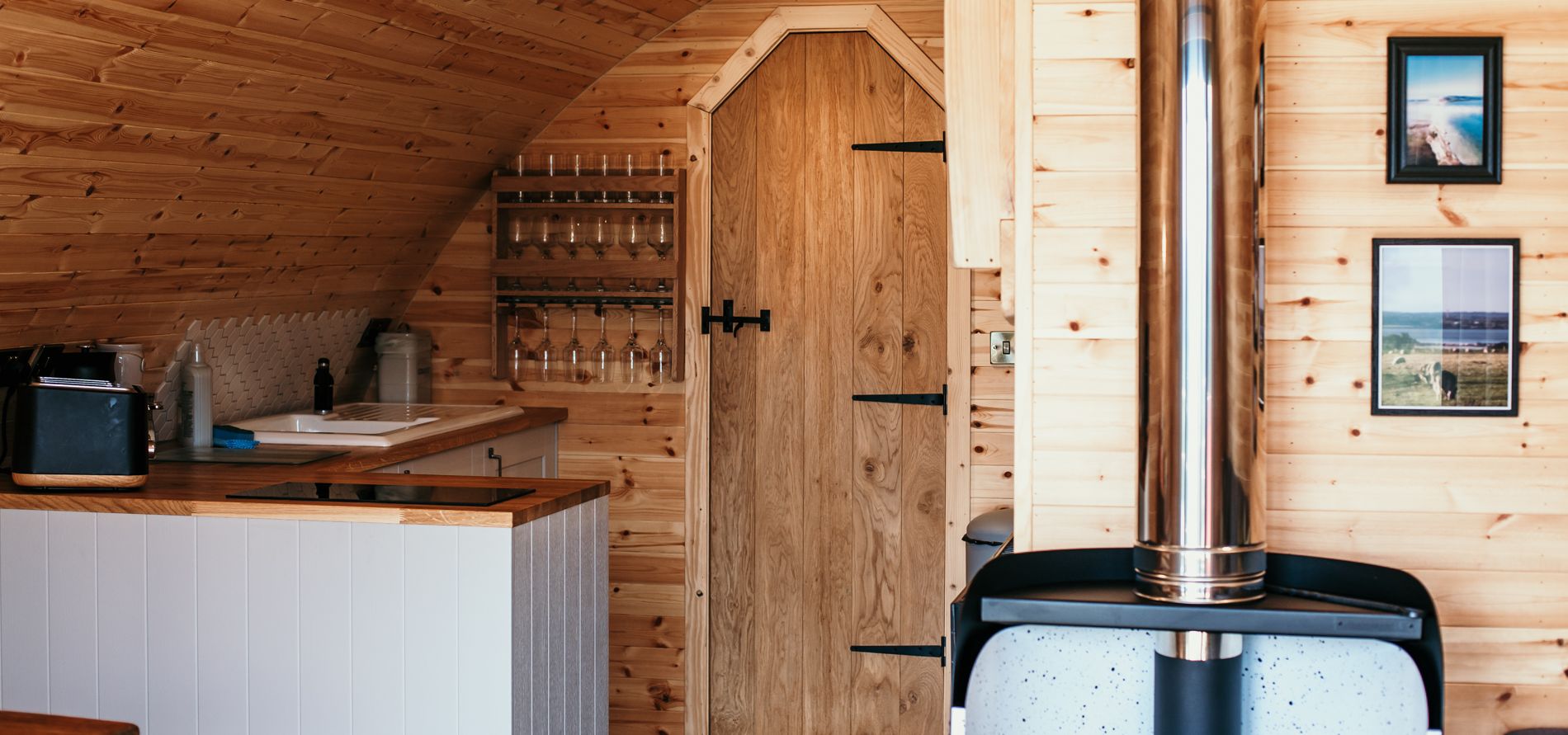 Wood-panelled cabin interior with small kitchenette, arched ceiling and log burner