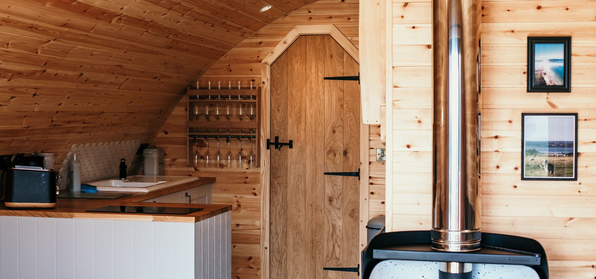 Wood-panelled cabin interior with small kitchenette, arched ceiling and log burner