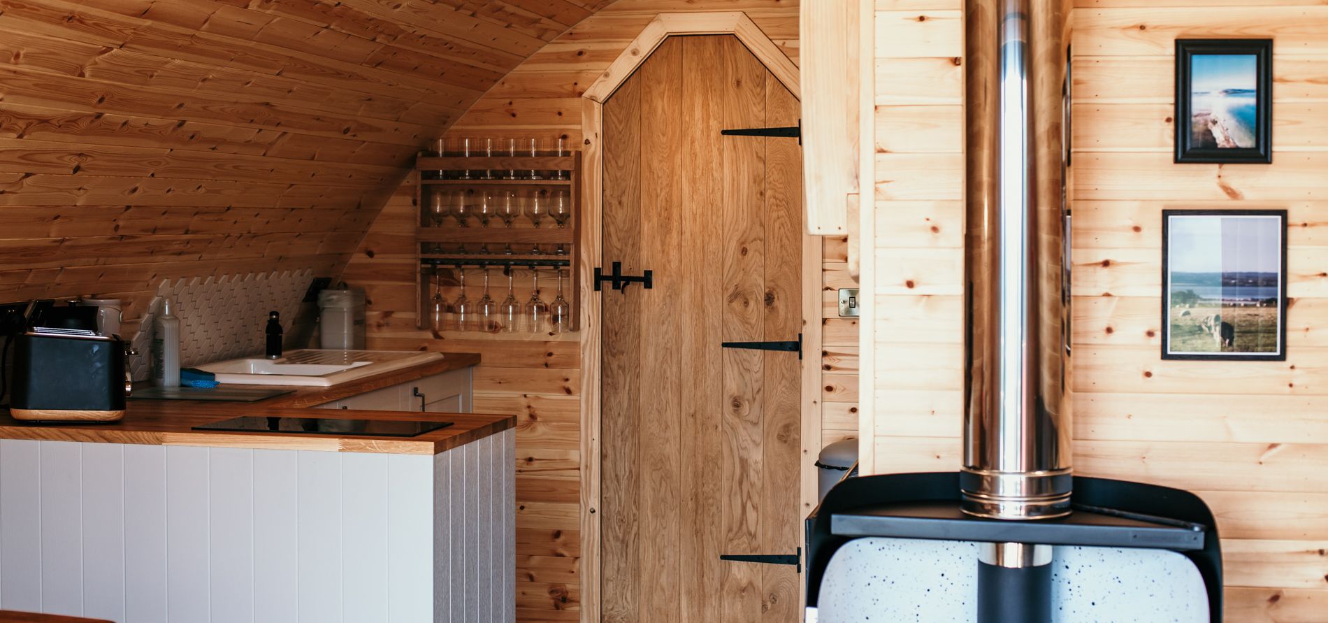 Wood-panelled cabin interior with small kitchenette, arched ceiling and log burner