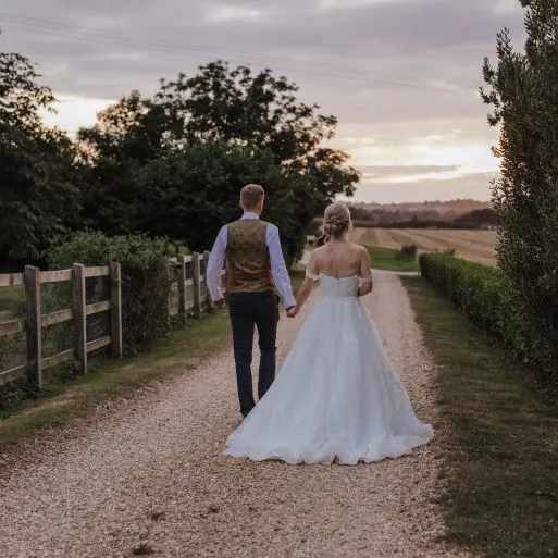 Bride and groom walking hand in hand down a gravel country lane at sunset