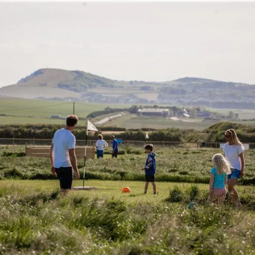 Family playing football golf on a grassy course with countryside hills in the background