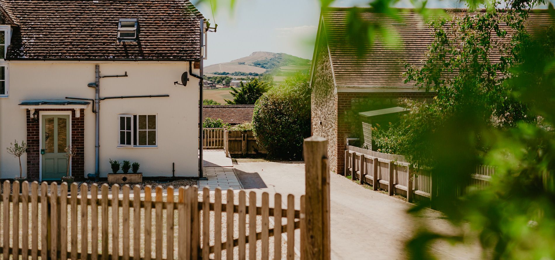 Exterior view of Tapnell Farm Dairyman's Cottage with a whitewashed house, farm buildings and distant hills