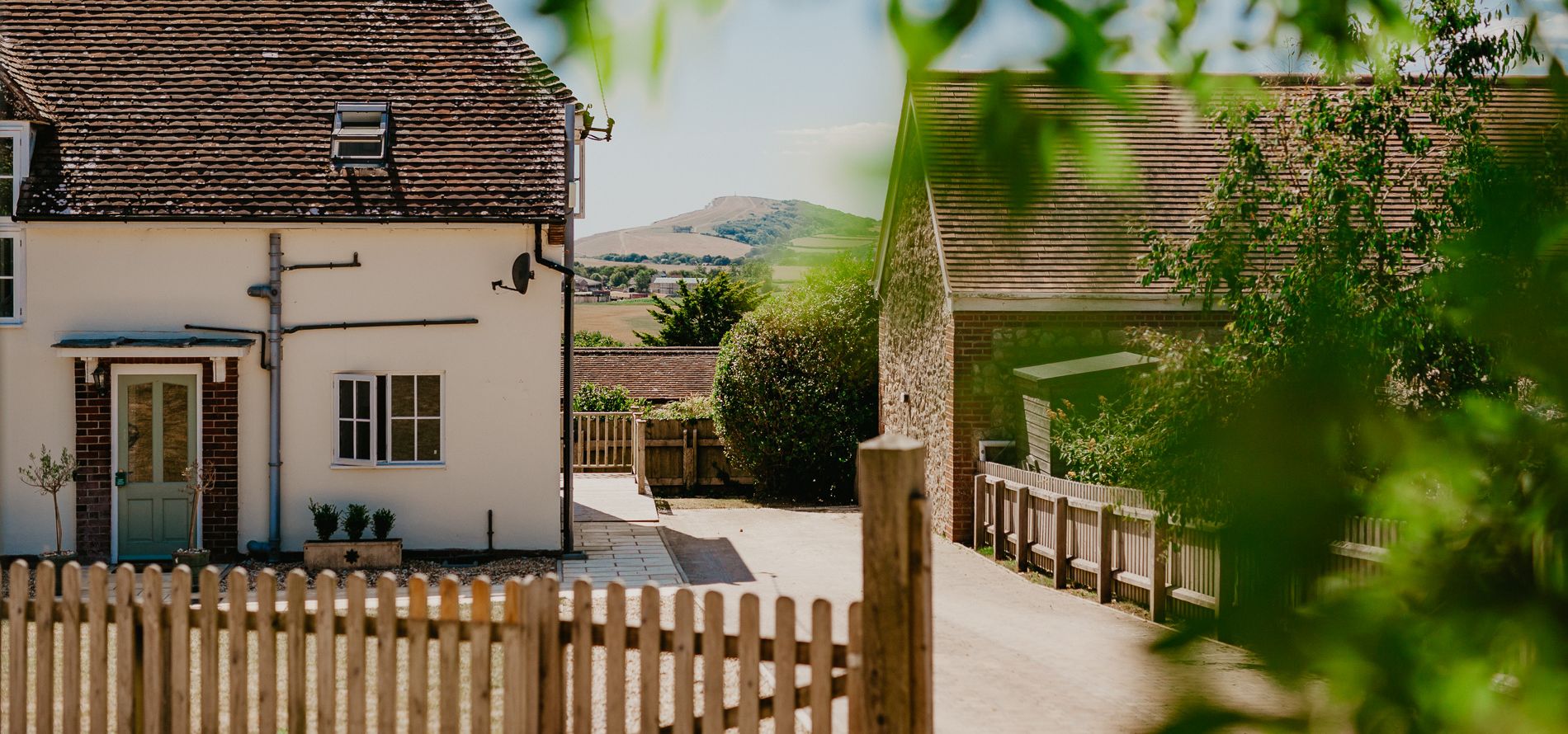 Exterior view of Tapnell Farm Dairyman's Cottage with a whitewashed house, farm buildings and distant hills