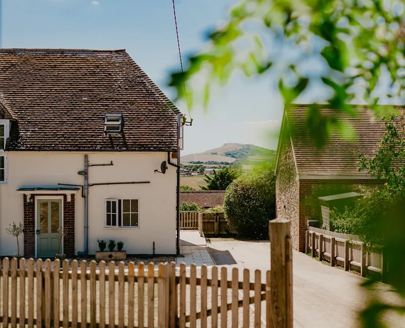 Exterior view of Tapnell Farm Dairyman's Cottage with a whitewashed house, farm buildings and distant hills