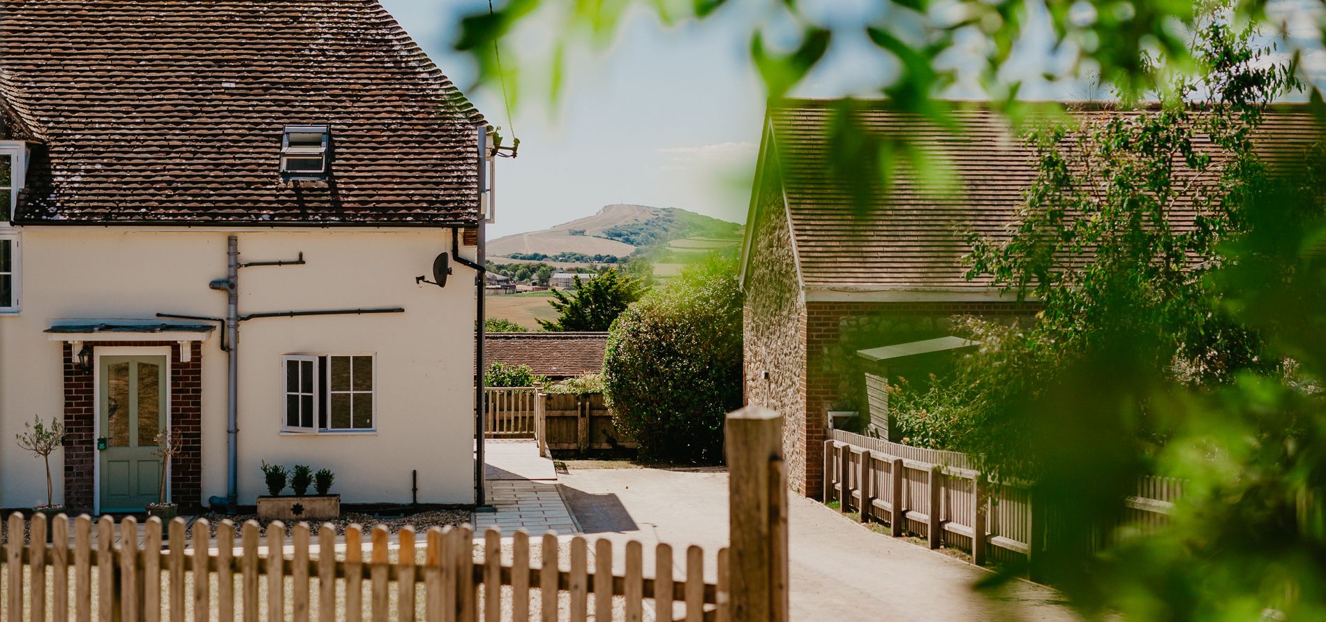 Exterior view of Tapnell Farm Dairyman's Cottage with a whitewashed house, farm buildings and distant hills