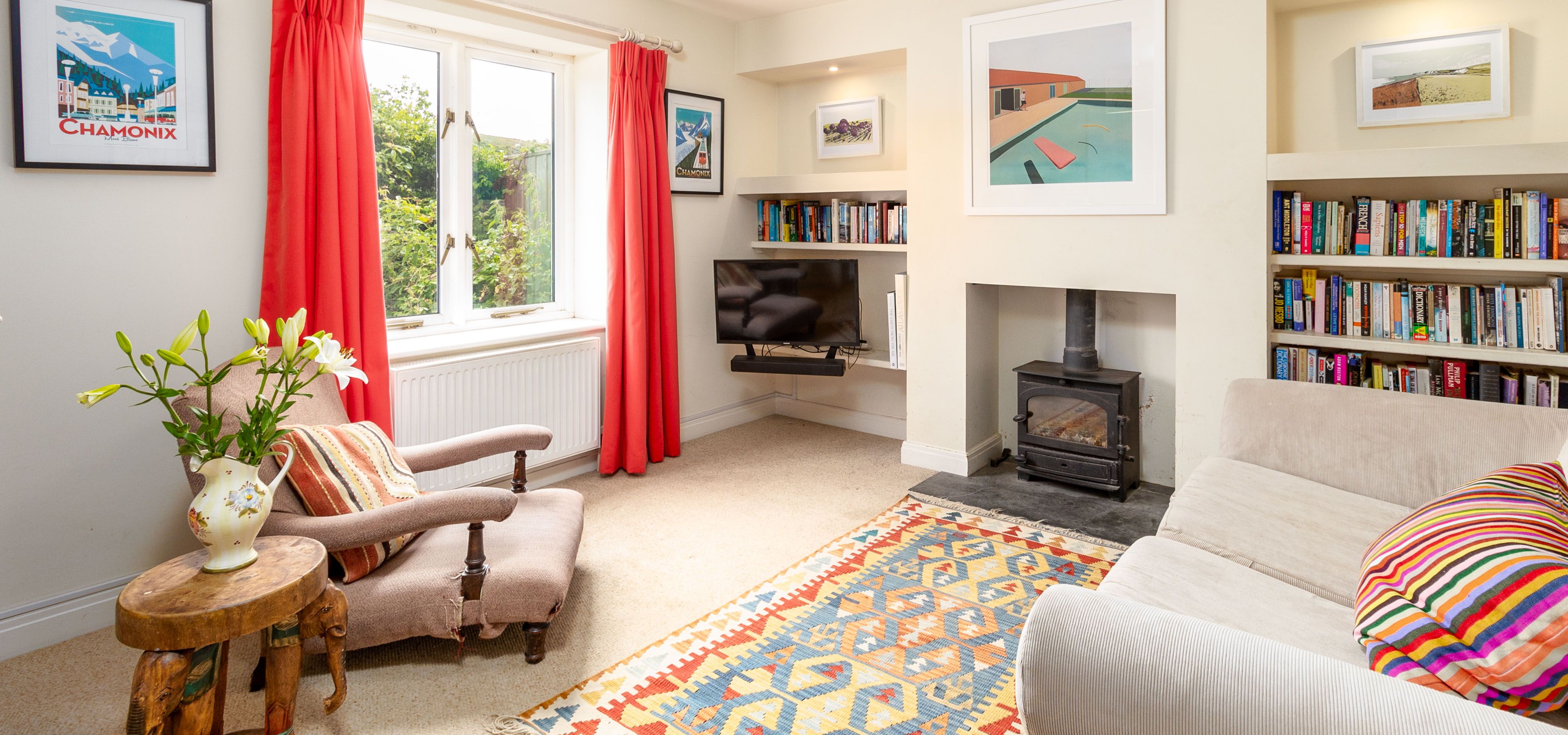 Bright living room with red curtains, wood-burning stove, bookshelves and patterned rug
