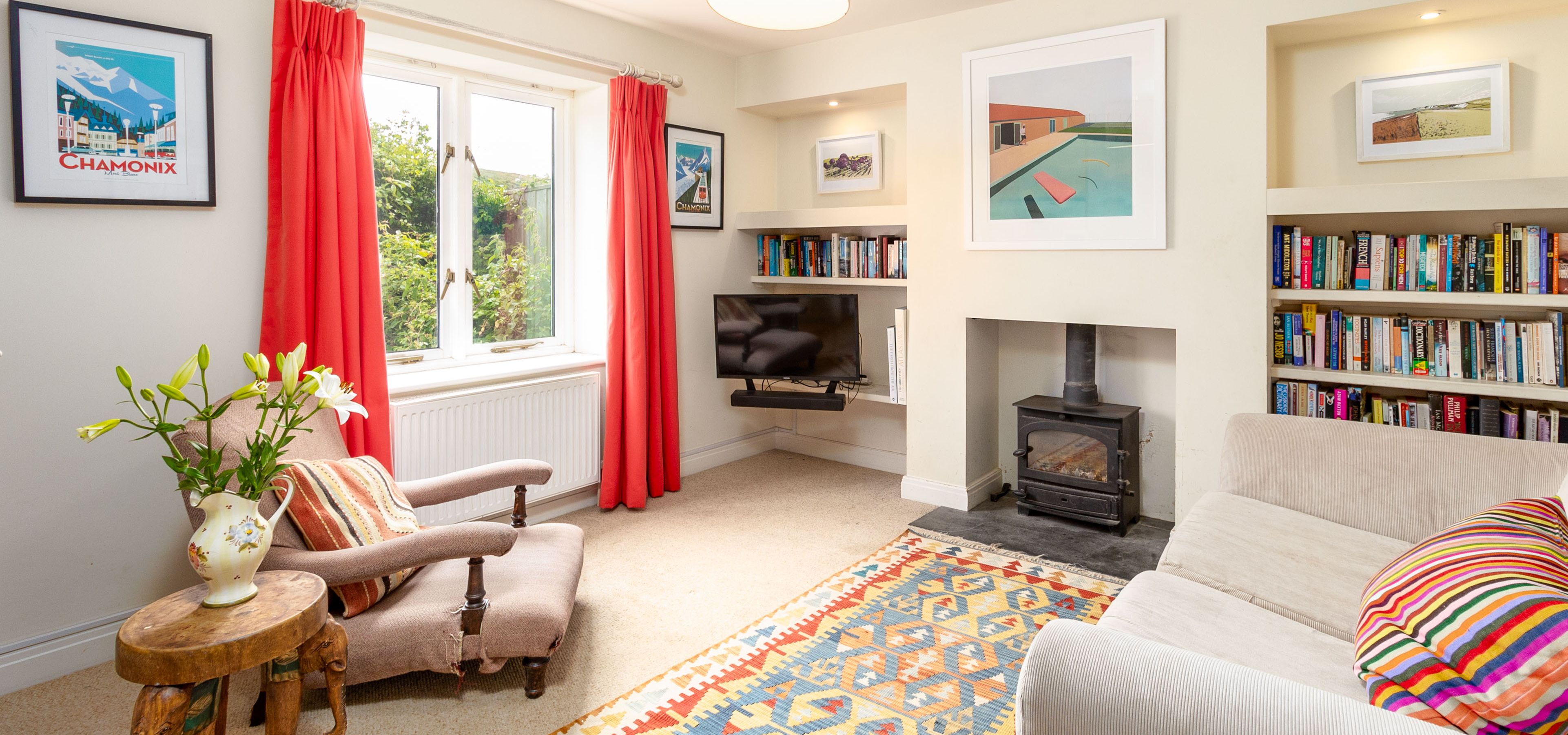 Bright living room with red curtains, wood-burning stove, bookshelves and patterned rug