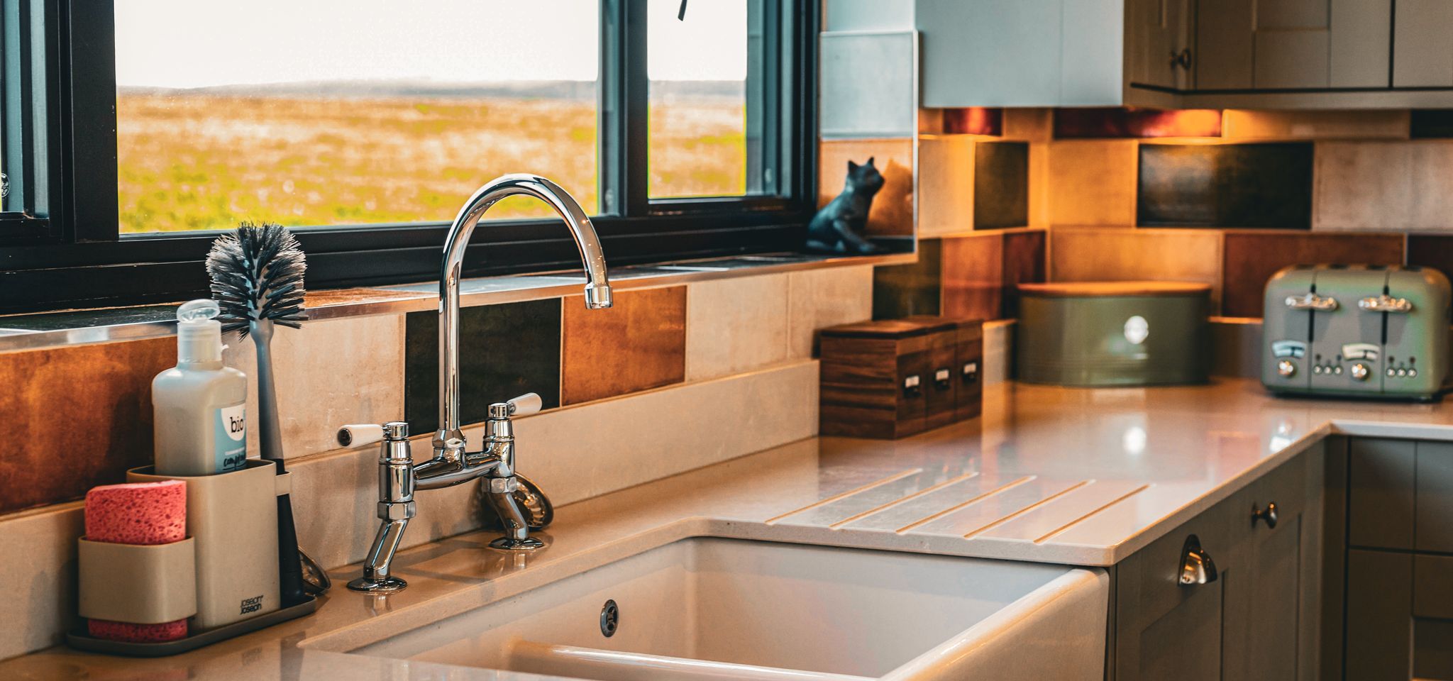 Modern kitchen sink with chrome tap beneath a window, with tiled splashback and countertop appliances
