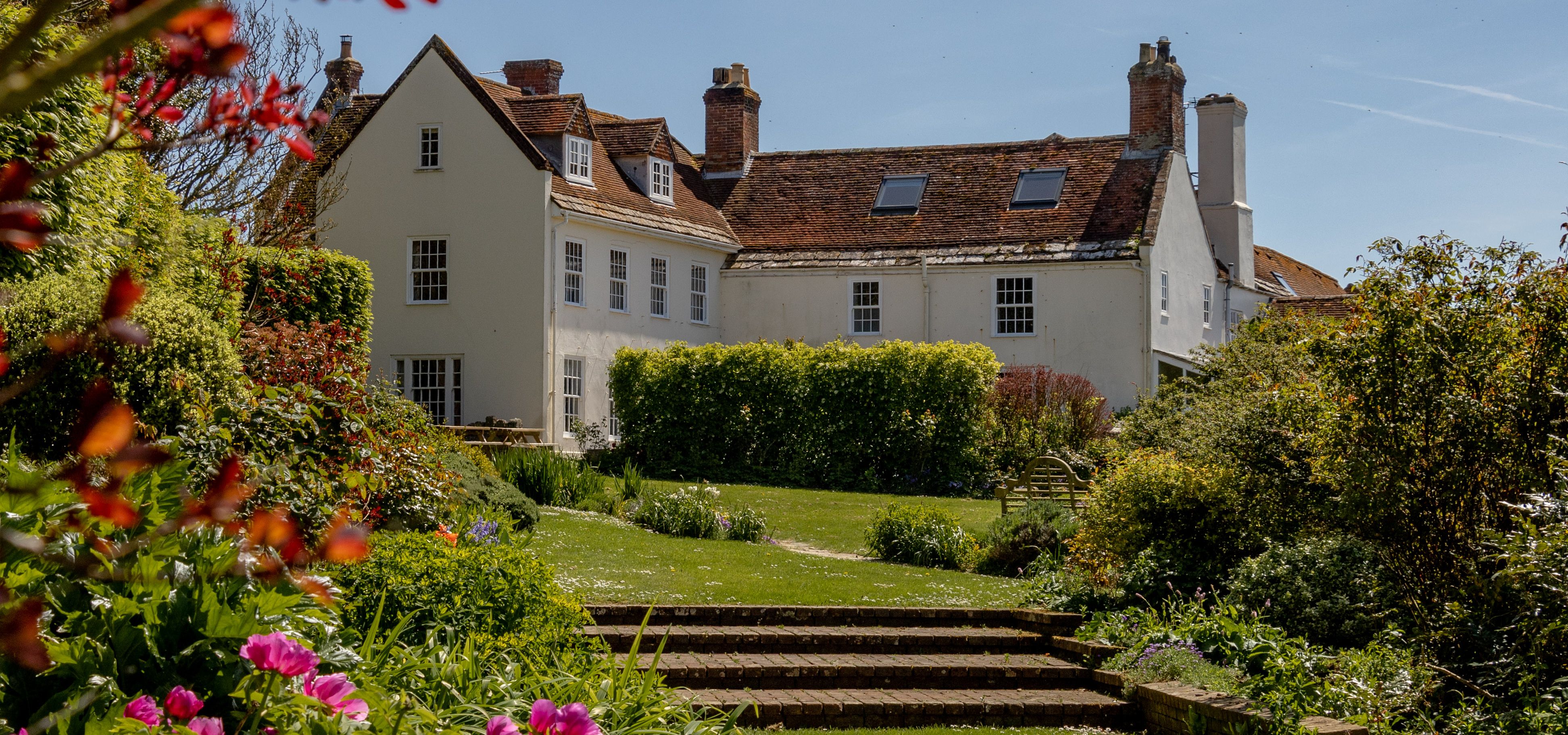Tapnell Manor house with a sunny garden, lawn and pink flowers in the foreground