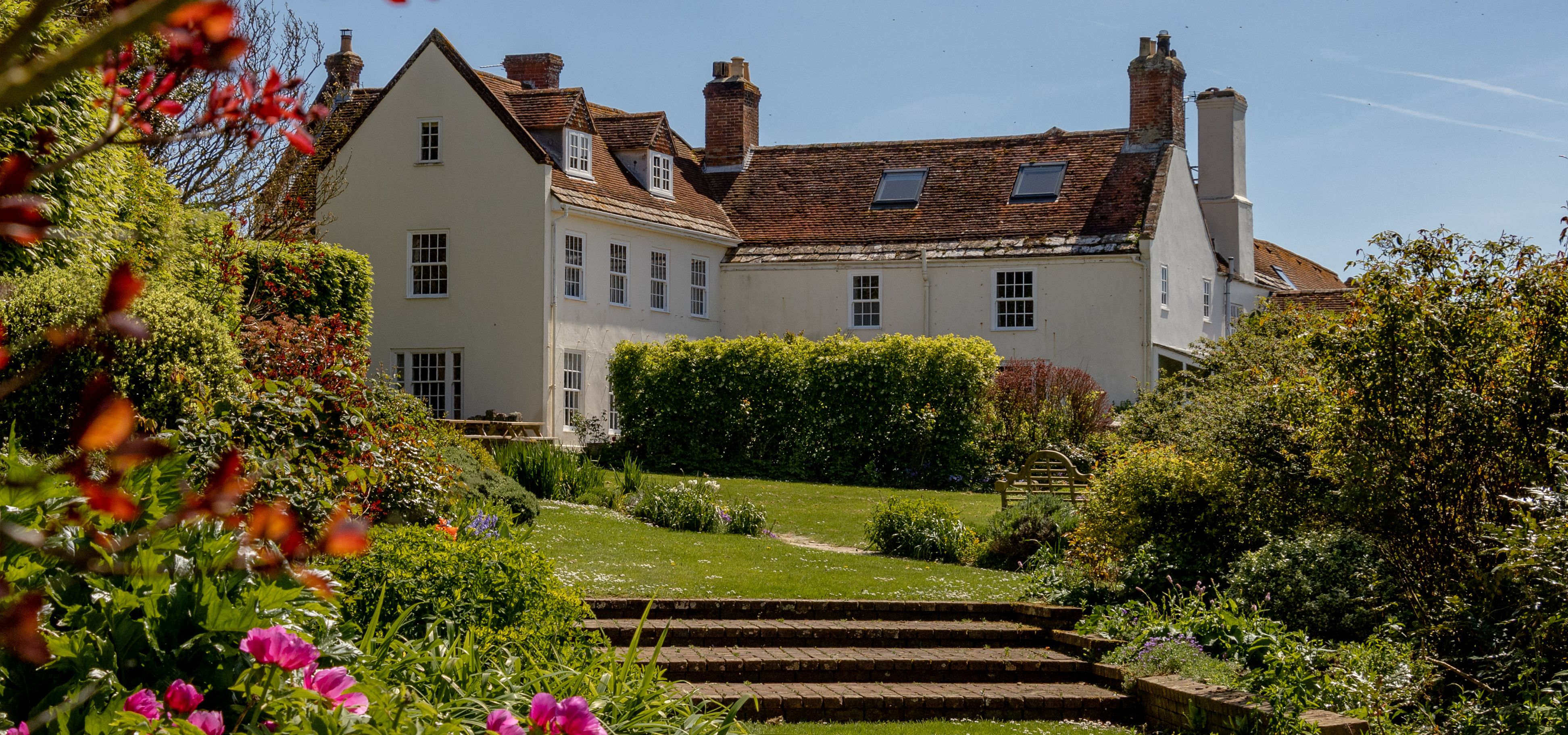 Tapnell Manor house with a sunny garden, lawn and pink flowers in the foreground