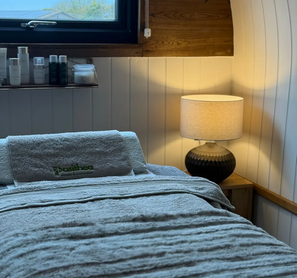 Cosy treatment room with massage bed, towels, lamp and window