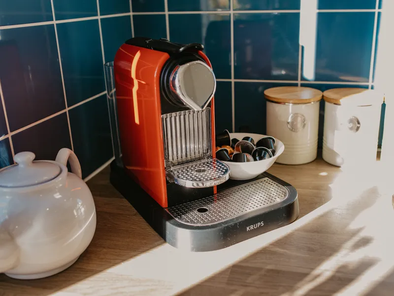 Red coffee pod machine on a wooden kitchen worktop beside cream storage jars and a bowl of capsules