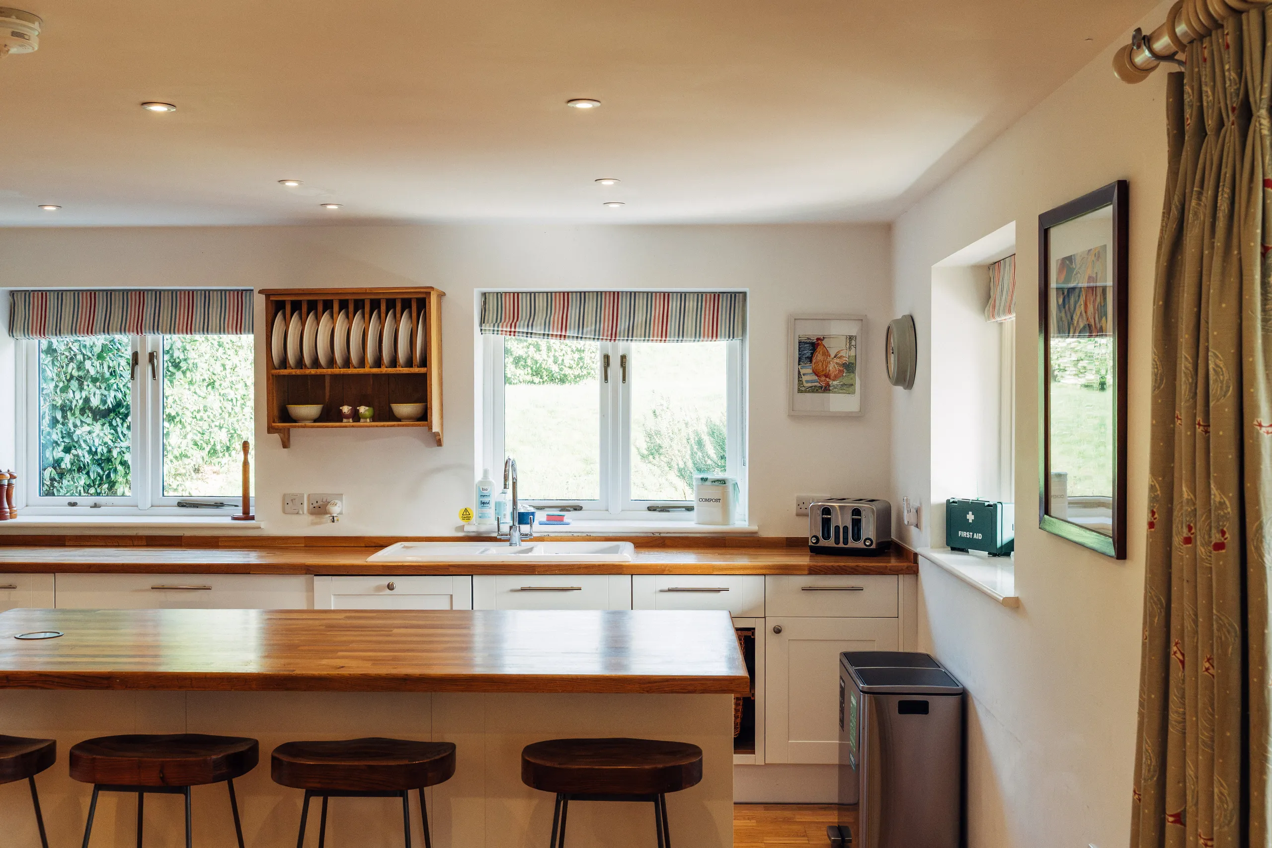 Bright farmhouse-style kitchen with wooden worktops, island seating and striped Roman blinds