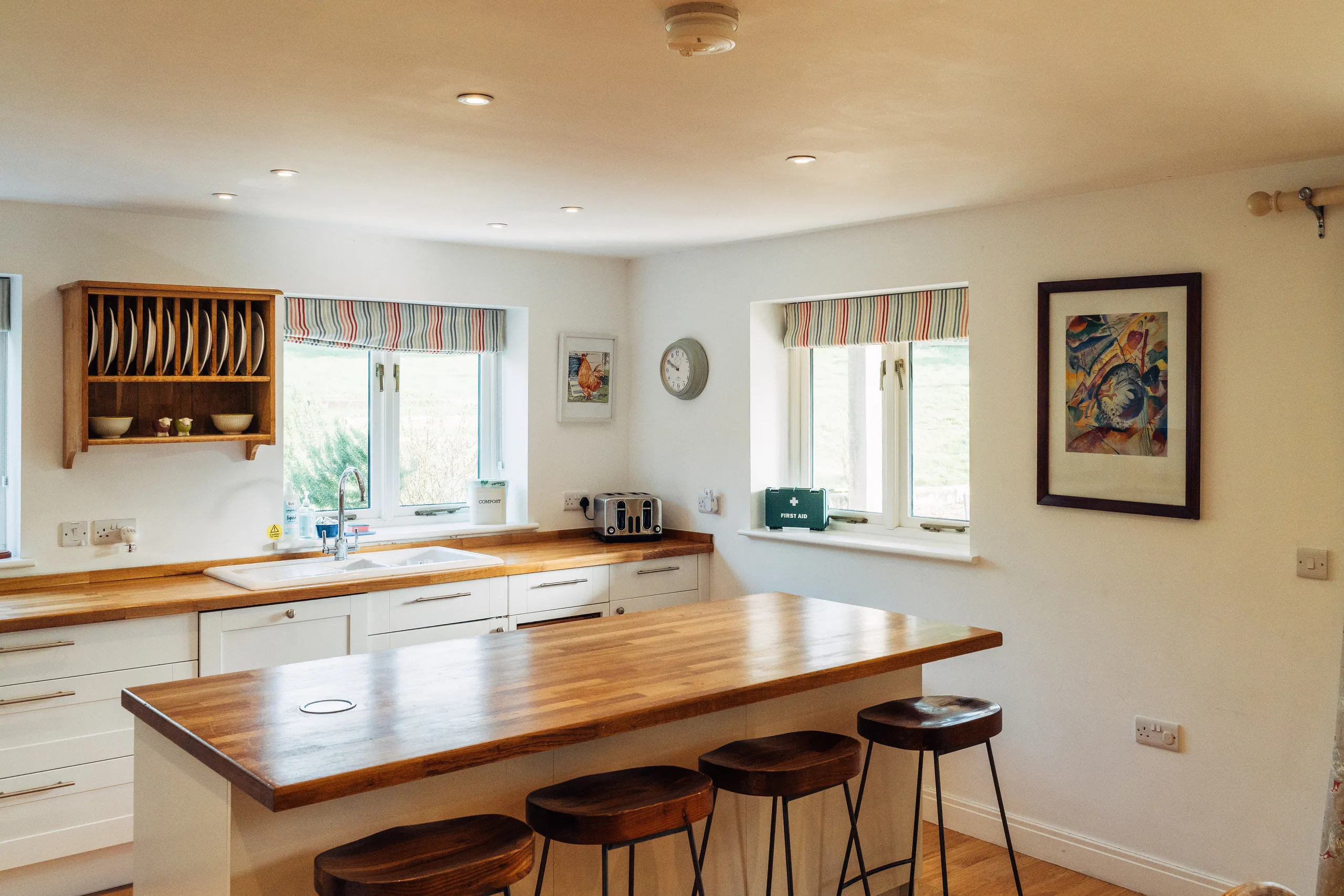 Bright country kitchen with wooden worktops, breakfast bar and striped Roman blinds