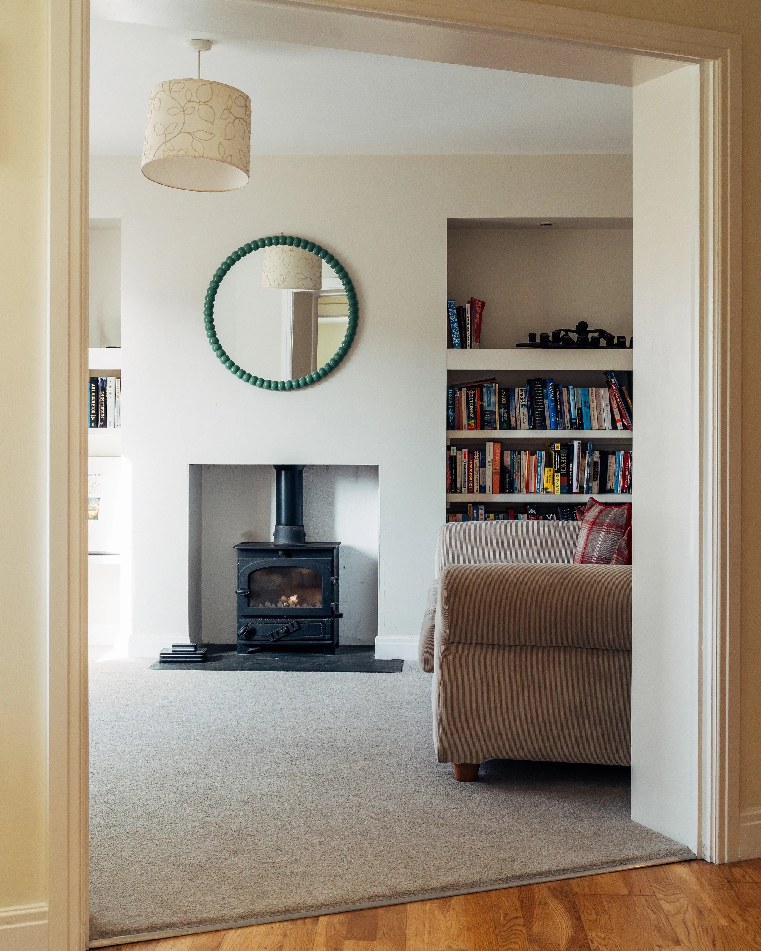 Cosy living room with a wood-burning stove, built-in bookshelves and a round green-framed mirror