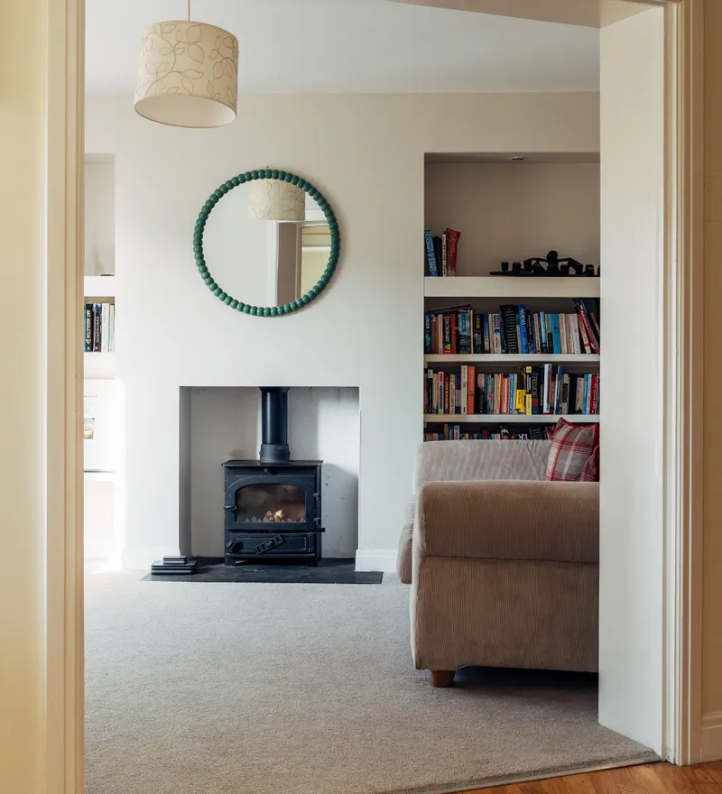 Cosy living room with a wood-burning stove, built-in bookshelves and a round green-framed mirror