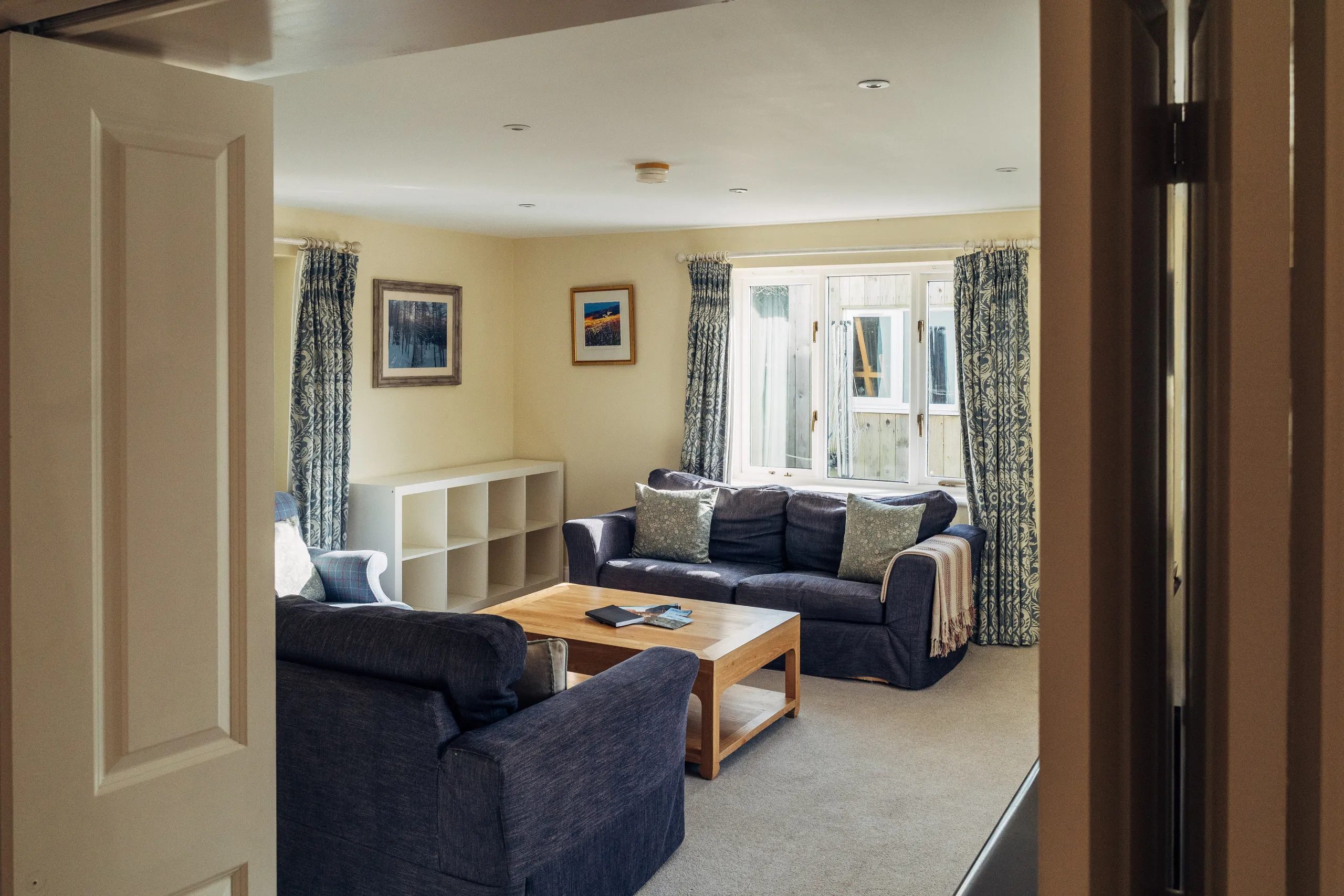Cosy living room with blue sofas, patterned curtains and a wooden coffee table