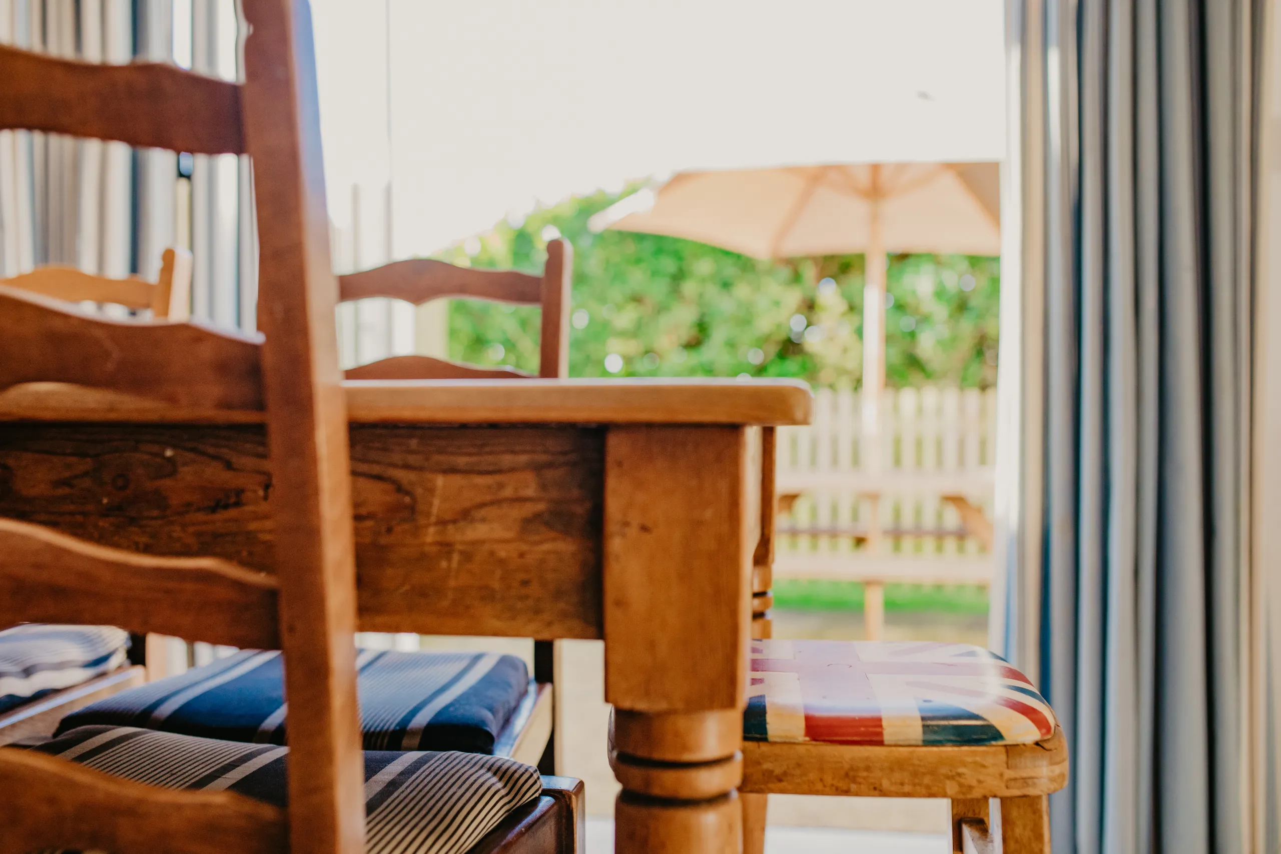 Wooden dining table and chairs by open patio doors, with a garden umbrella outside