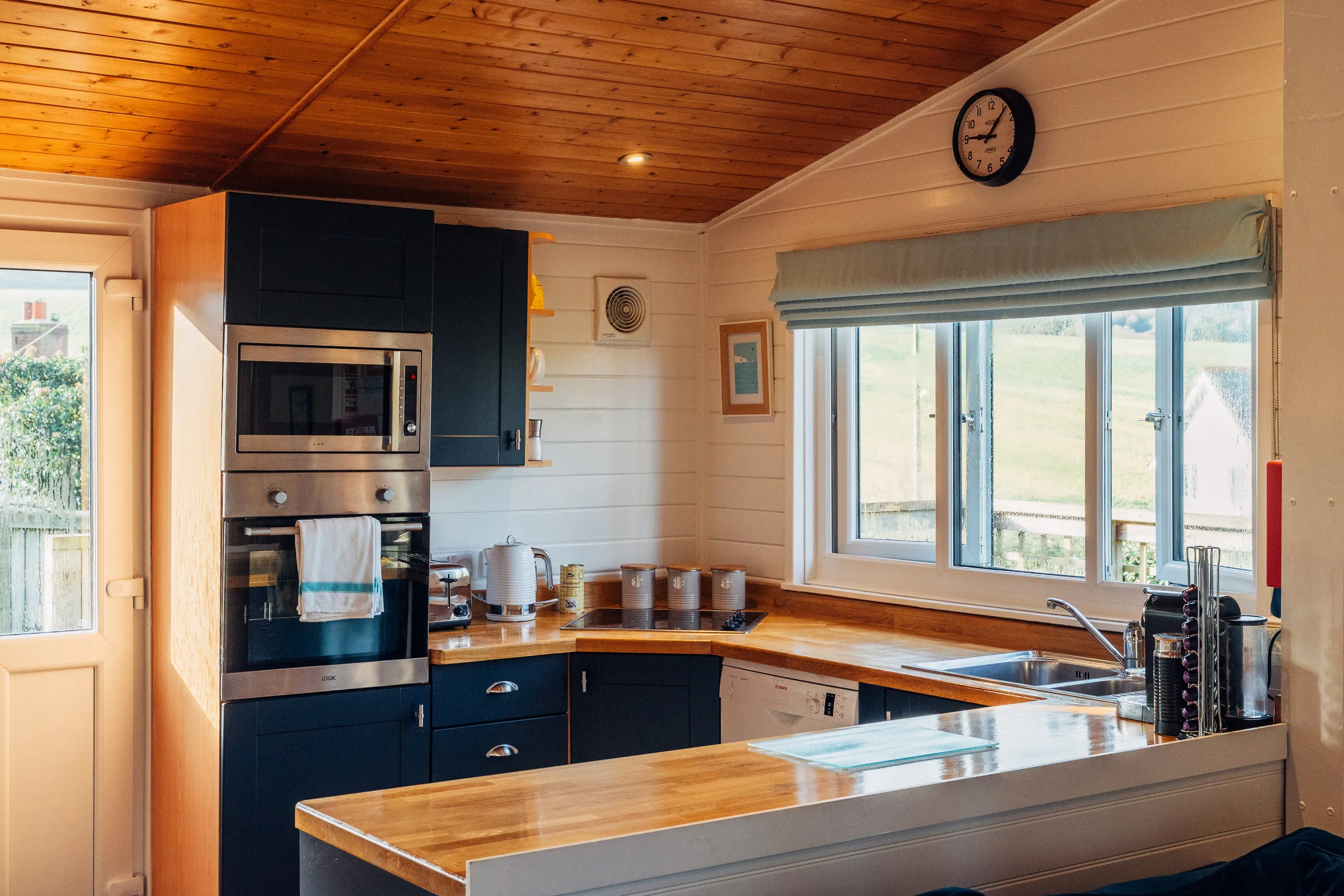 Cosy lodge kitchen with navy cupboards, wooden worktops, built-in oven and large window