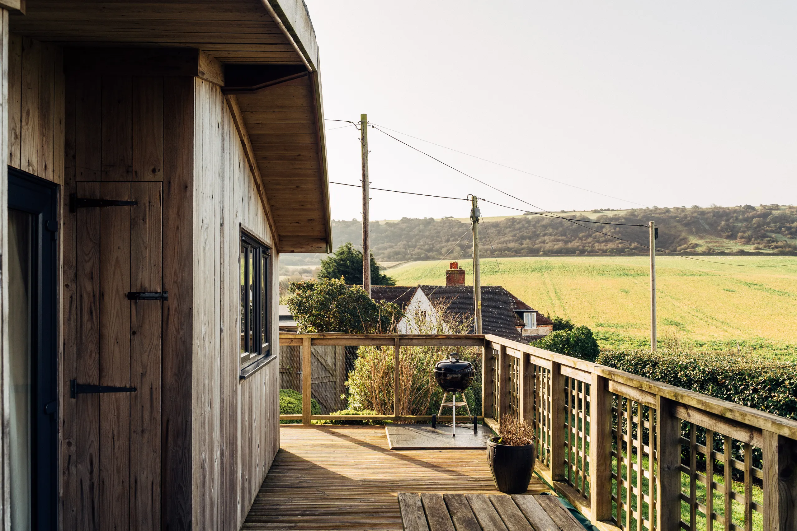 Timber-clad cabin with a wooden deck and barbecue overlooking rolling countryside fields.