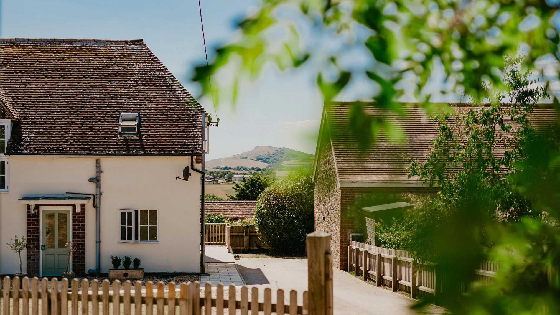 Exterior of Dairyman's Cottage at Tapnell Farm with a picket fence, driveway and countryside views.
