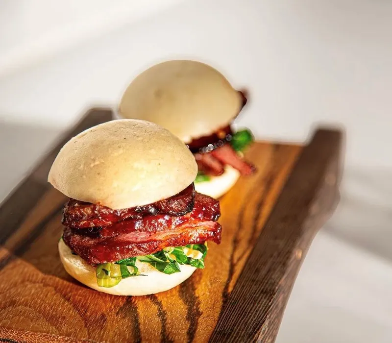 Two smoked meat bao buns on a wooden serving board